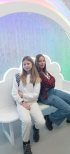 Dwie dziewczyny pozują do zdjęcia na ławce w kształcie białej chmurki