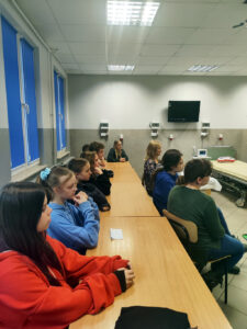 Grupa uczniów siedzi na krzesłach w pomieszczeniu wyglądającym na ambulatorium