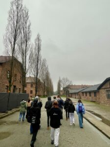 Grupa uczniów spaceruje między blokami w obozie zagłady Auschwitz
