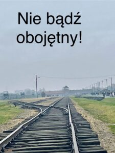 Tory kolejowe, wartownia i brama główna Auschwitz II. Na zdjęciu umieszczono napis "Nie bądź obojętny"