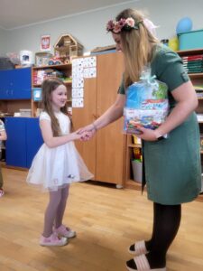 Dziewczynka przyjmuje od przedszkolanki nagrodę za udział w konkursie