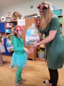 Dziewczynka przyjmuje od przedszkolanki nagrodę za udział w konkursie