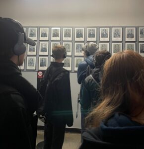 Uczniowie oglądają zawieszone na ścianie zdjęcia więźniów Oświęcimia